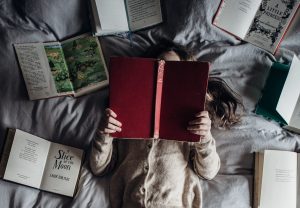 A teenager is surrounded by books while reading.