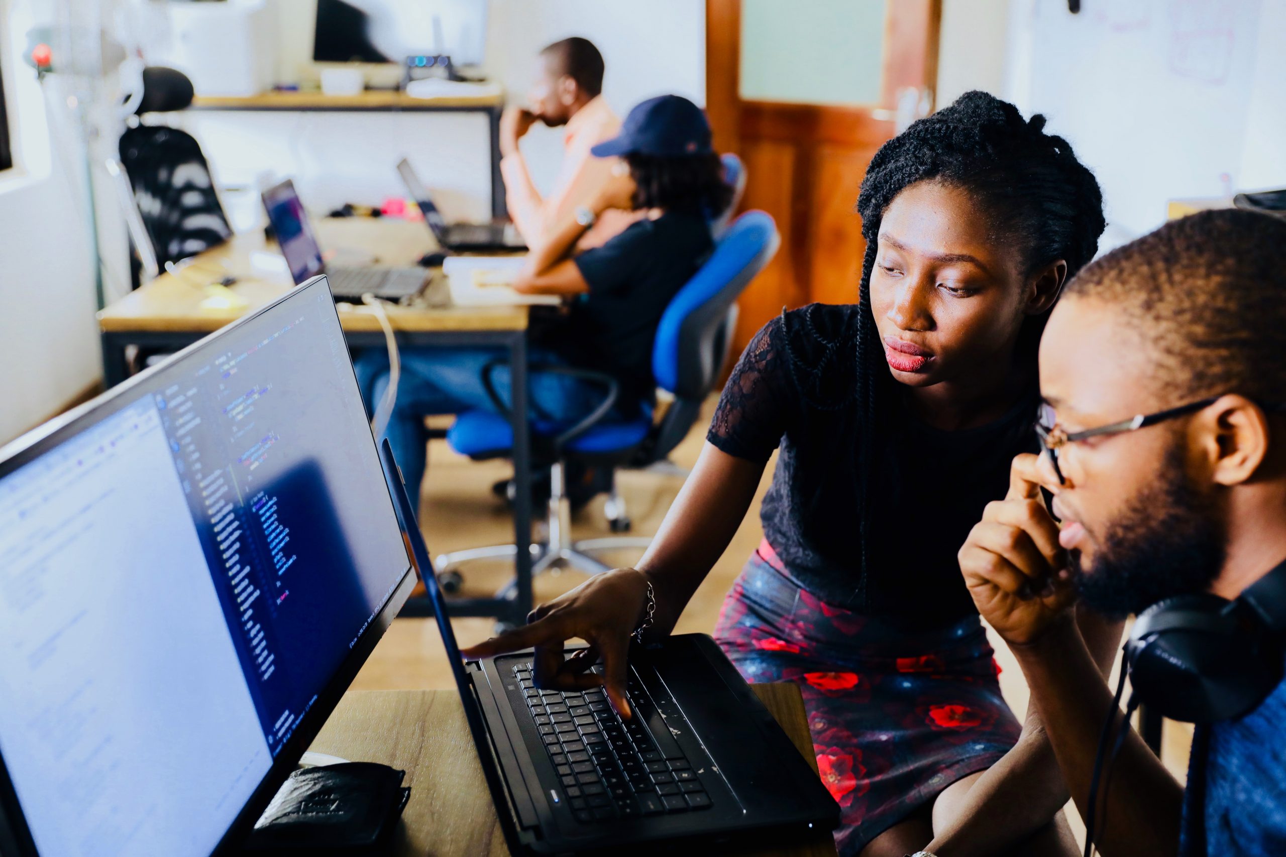 woman and man sitting in front of a monitor helping each other