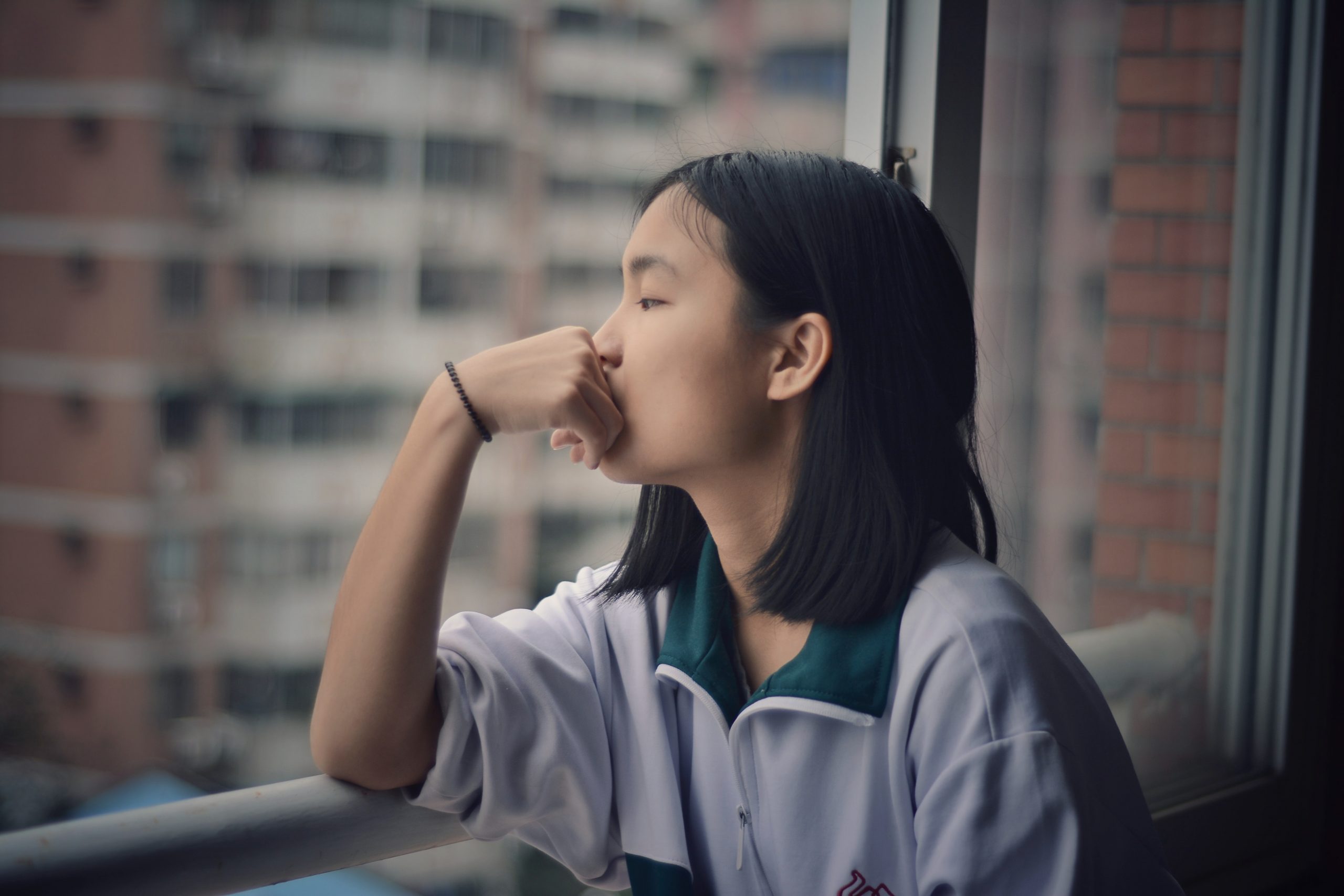 Woman with her elbow resting on a windowsill with her hand on her chin. She is looking out of the window.