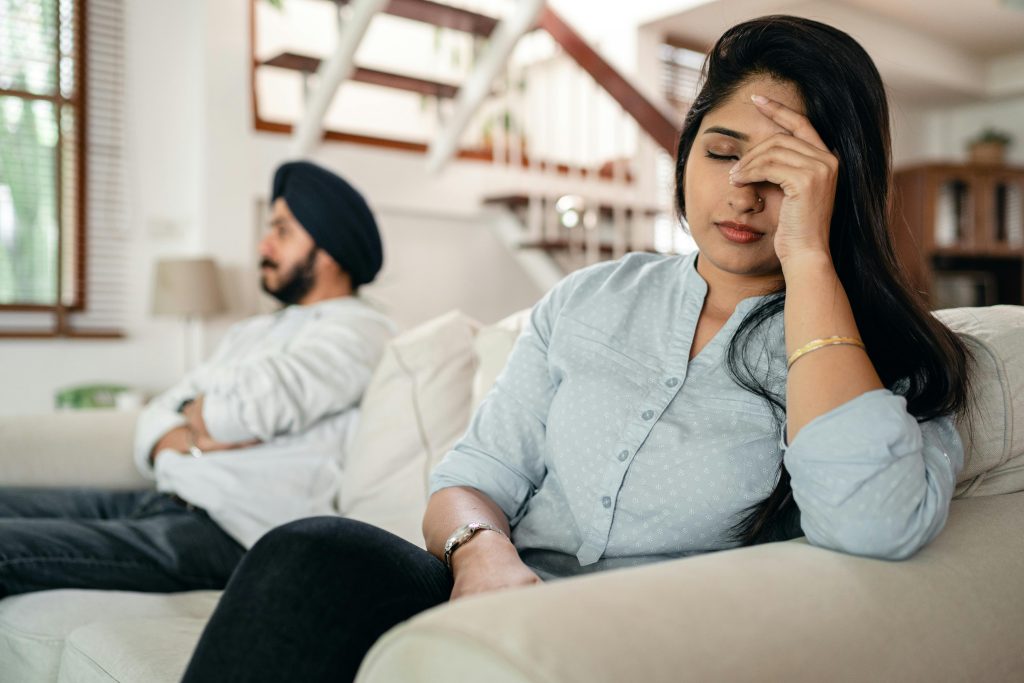 A man and a woman on a couch looking upset and away from each other.