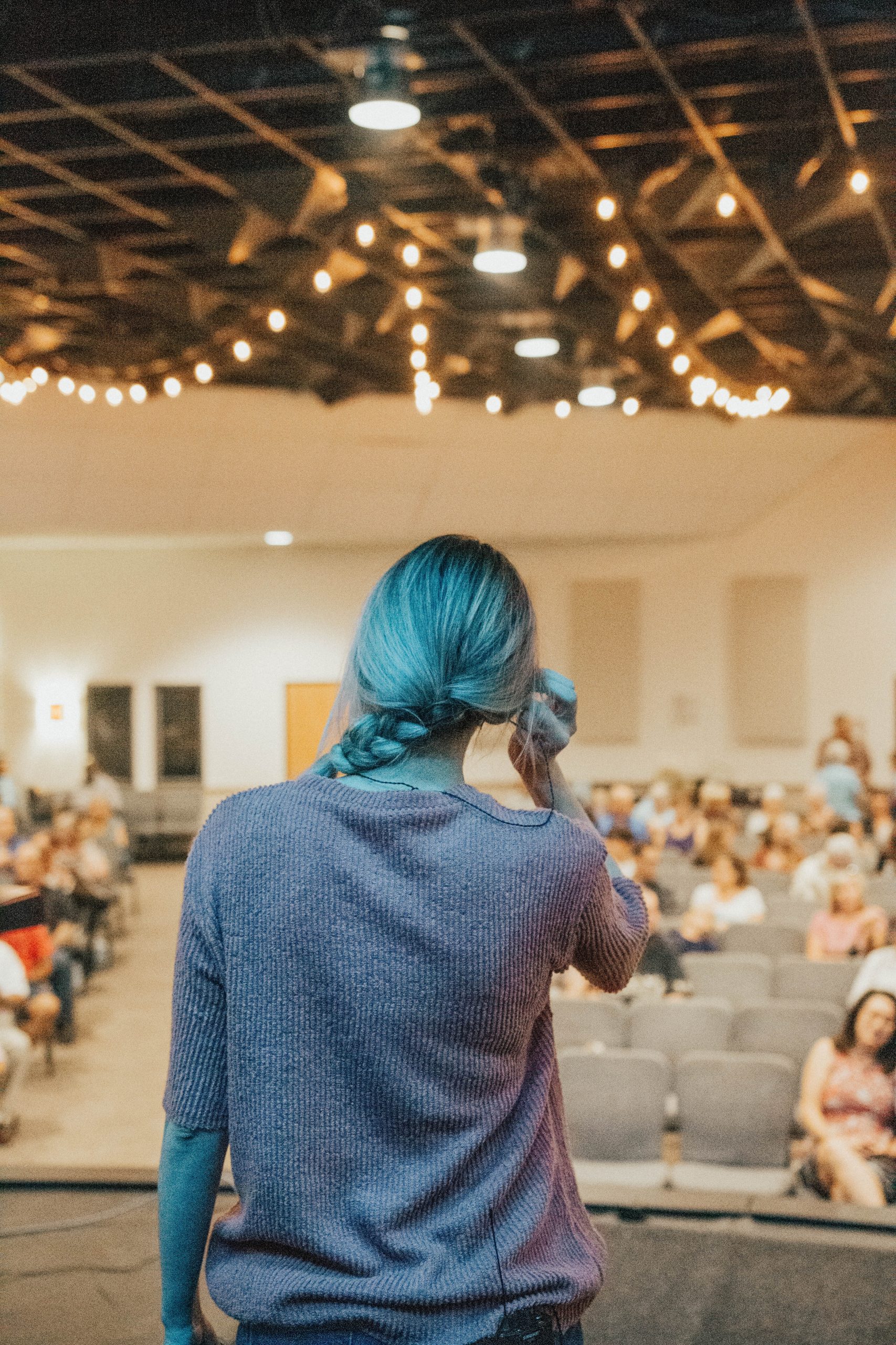 Photograph from stage view of a woman tucking her hair behind her ear. There's people in the audience.