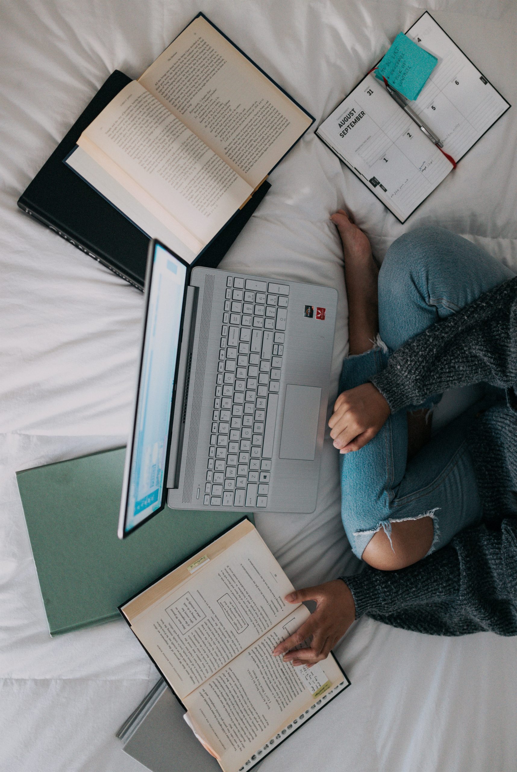 Aerial photograph of a woman sitting on the bed with papers and a laptop spread out in ffront of her.