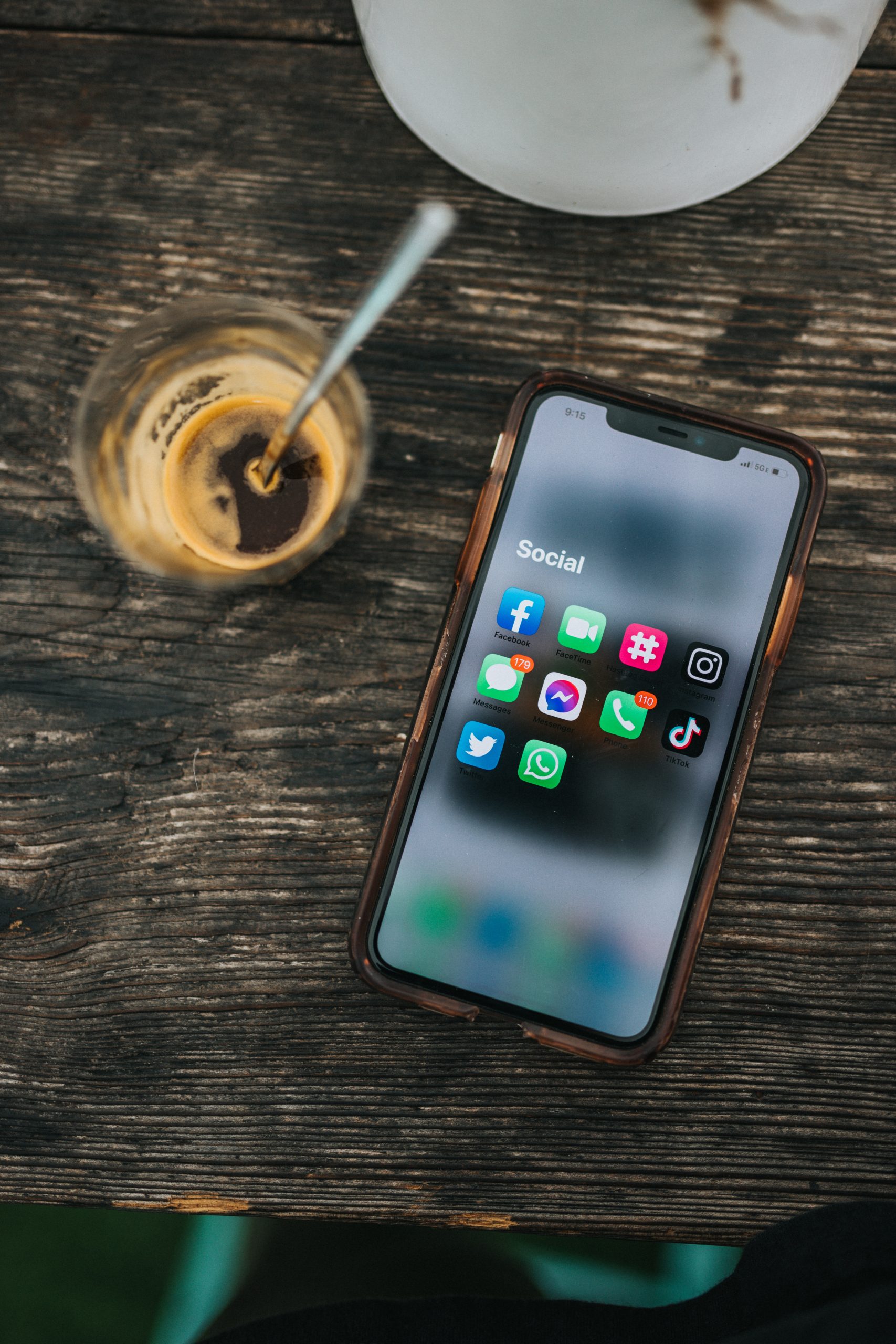 Aerial photograph of an iPhone on a table with "Social" folder open containing Facebook, Facetime, TikTok, Messages, Phone, Facebook messenger, Twitter, WhatsApp, and other apps.