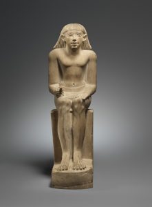 Limestone sculpture of Idi, a seated man with an animated face and his hands in his lap.