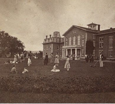 Photograph of a building and with people on the front lawn at the Oneida Commune