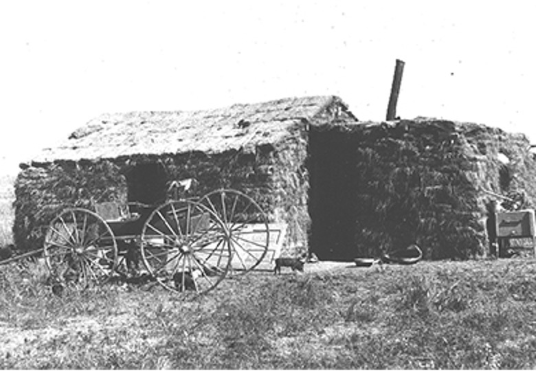 Photograph of a sod house with a wagon sitting in front of the door