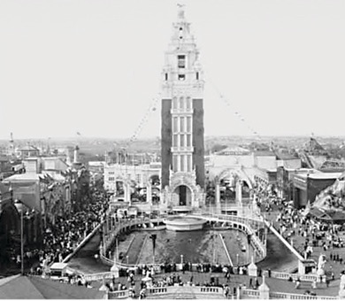 A photograph of Dreamland Amusement Park tower at Coney Island. You can see the amusement park behind the tower and there are people milling about the park.