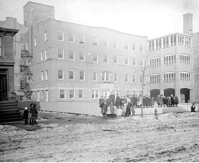A photograph of Hull house with settlement house workers and children standing in front.