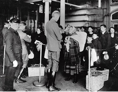 Photograph of an immigration inspector examining immigrants who are lined up in front of him.