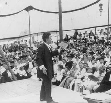 Photograph of Governor Robert “Fighting Bob” La Follette on a stage facing a crowd of people.