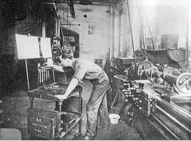 Photograph of a machinist working at his station in a factory.