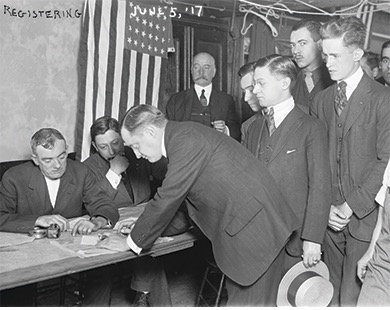 Photograph of men lined up in front of a table to volunteer. The man in the front is signing a document.