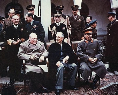 A color photo of Winston Churchill, Franklin D. Roosevelt, and Joseph Stalin seated together outdoors with other figures standing behind them. This is a photo from the Yalta Conference.