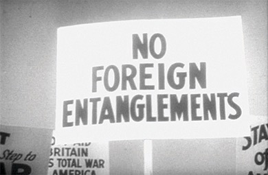 A close-up black and white photo of a sign that reads "NO FOREIGN ENTANGLEMENTS". Other signs are partially visible in the background.