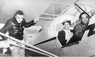 A black and white photo of three people next to a JP-3 Piper airplane. Director of Training at Tuskegee, Lewis Jackson is stepping into the cockpit, and seated inside are Eleanor Roosevelt and Black fighter pilot, Charles Alfred “Chief” Anderson.  All are smiling.