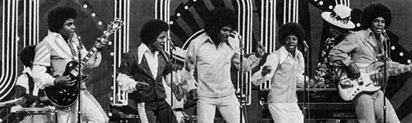 A black and white photo showing the Jackson 5 in coordinated outfits, performing on stage with musical instruments.
