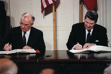 A color photo of Ronald Reagan and Mikhail Gorbachev sitting at a table signing the Intermediate-Range Nuclear Forces Treaty.