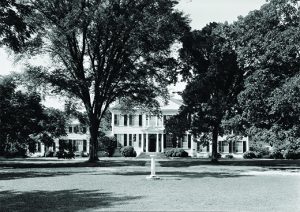 Image shows the exterior of an opulent southern home with lots of property in front.
